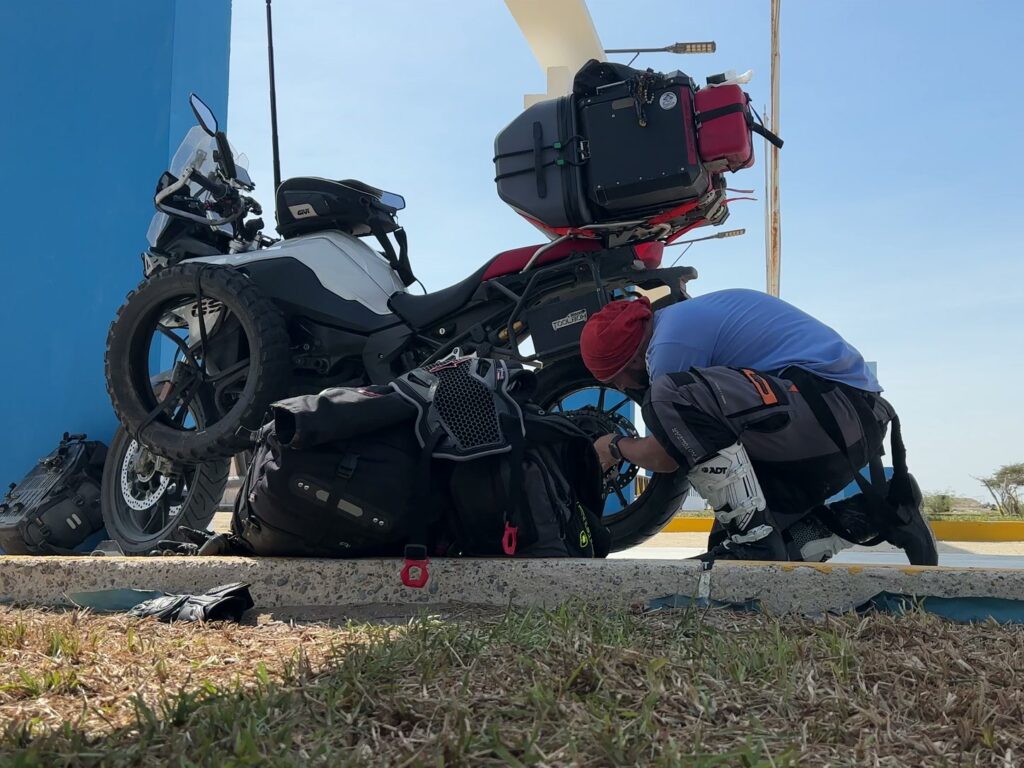 Un motoviajero revisa la rueda trasera de su moto junto al equipaje durante una parada.