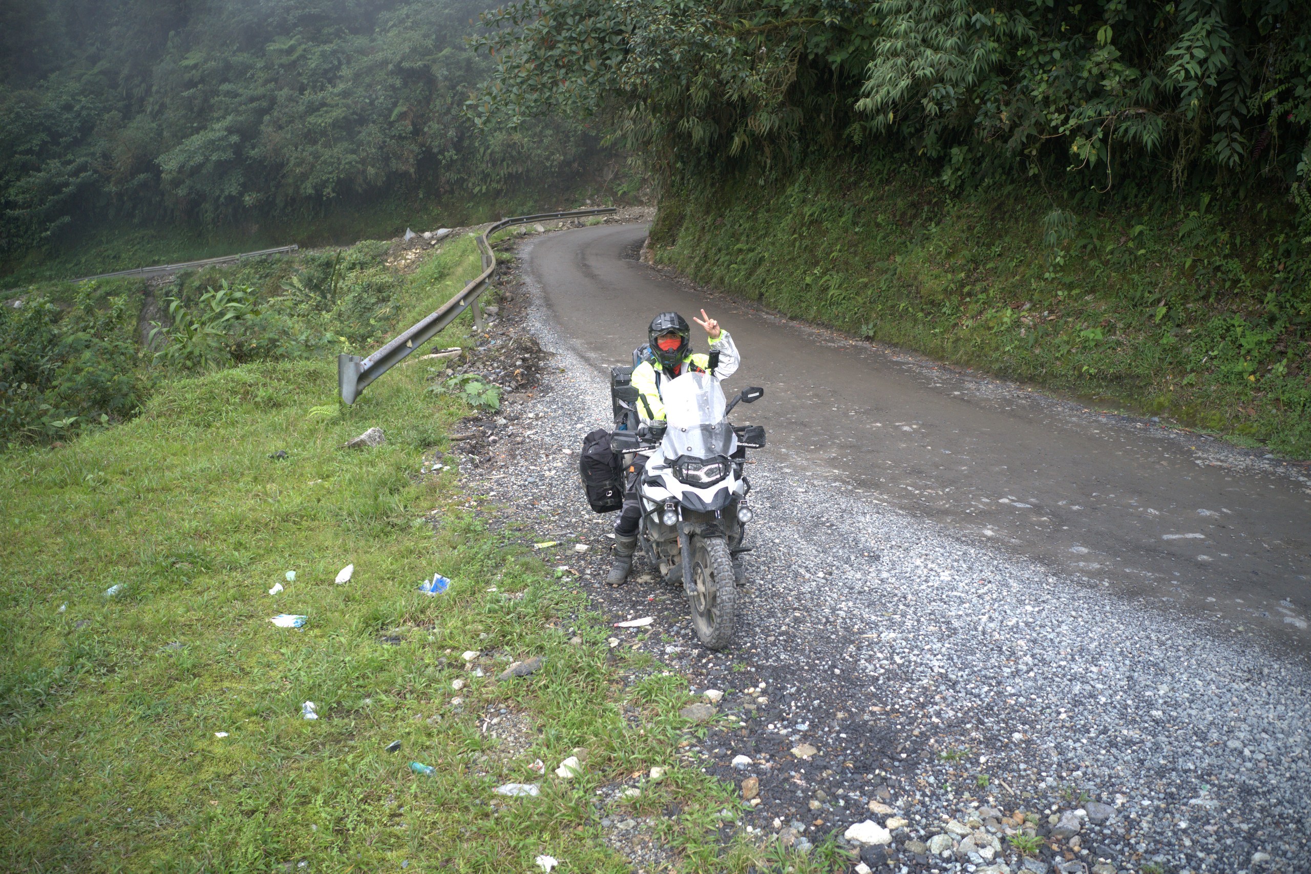 Juan Varner en su motocicleta sobre grava, junto a una curva estrecha y una ladera cubierta de vegetación.