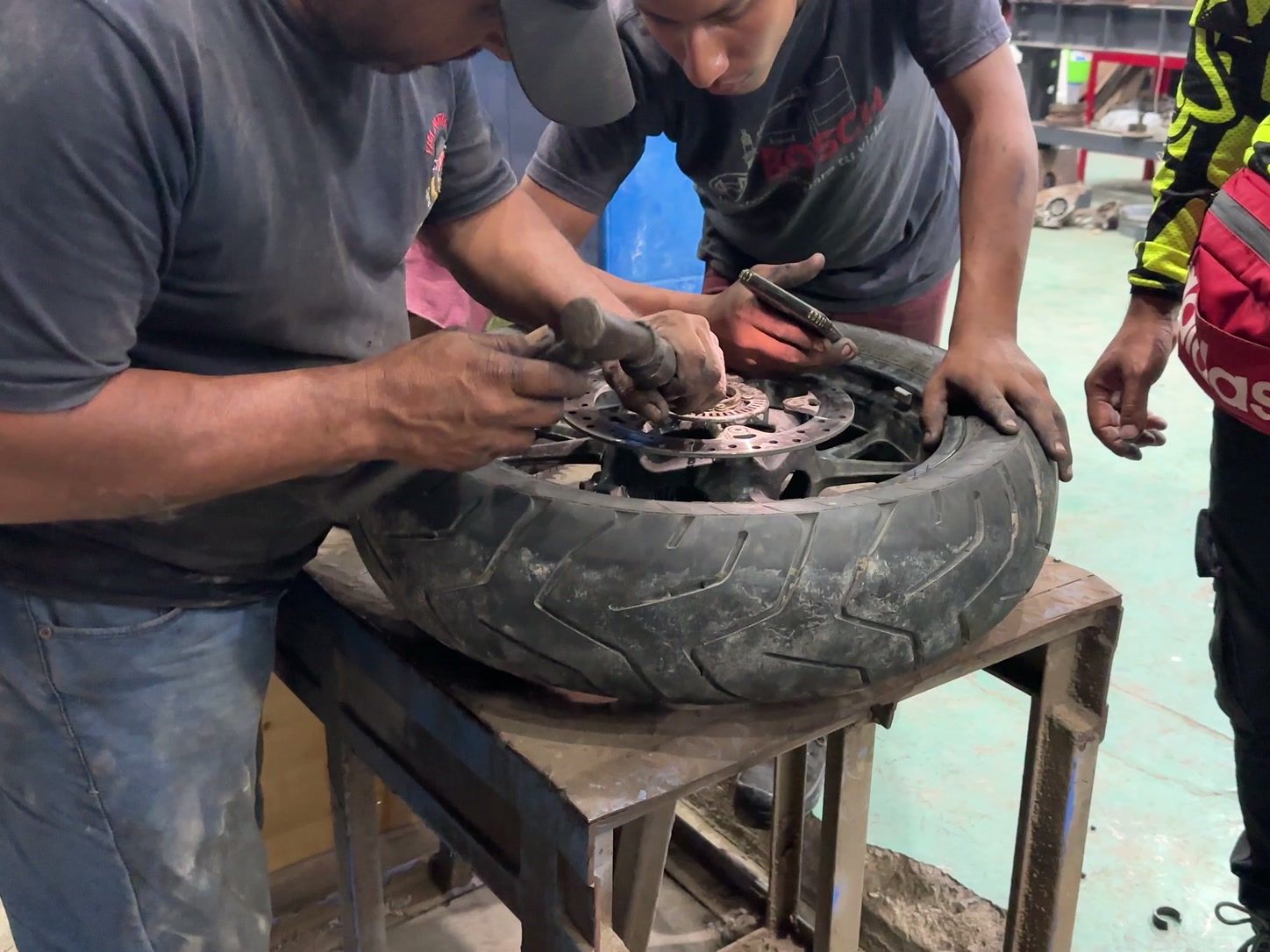 Varias personas trabajan con herramientas sobre la rueda en un taller.